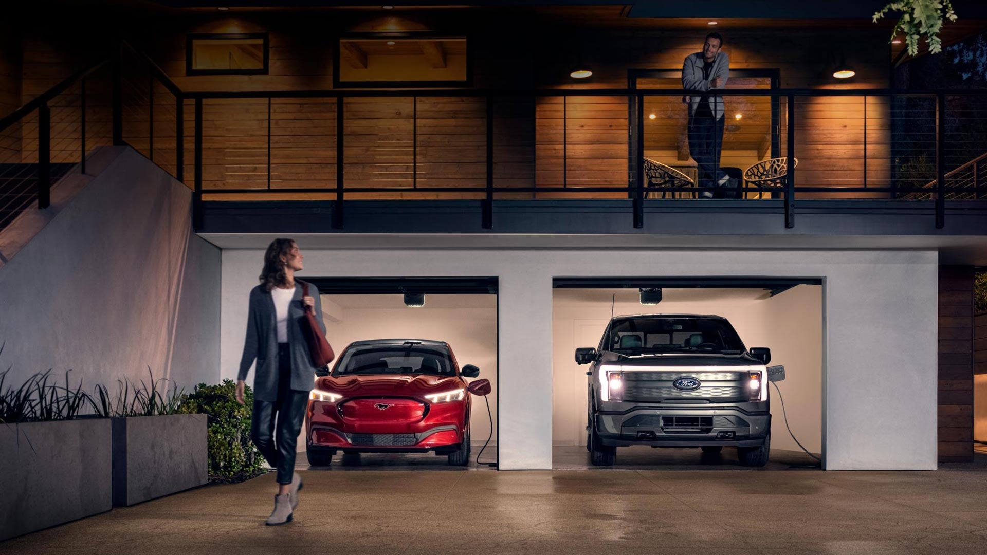 Woman walking out from home garage with a 2024 Mustang® Mach-E and Ford Lightning® truck in plugged-in and charging | Apple Autos in Apple Valley MN